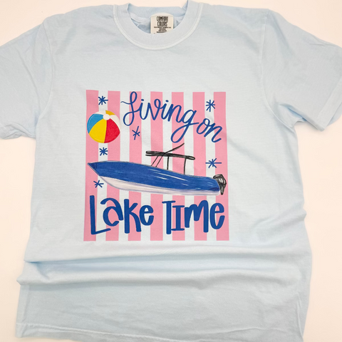 Light blue t-shirt with 'Living on Lake Time' graphic design featuring a boat and beach ball on a striped background.