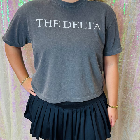 Person wearing a gray t-shirt with 'THE DELTA' text against a colorful, patterned background